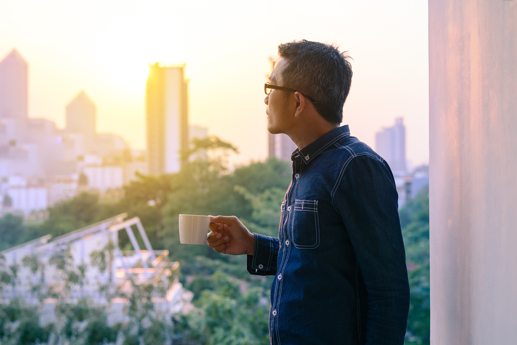 Businessman in denim jacket and glasses drinking hot coffee in sunrise.